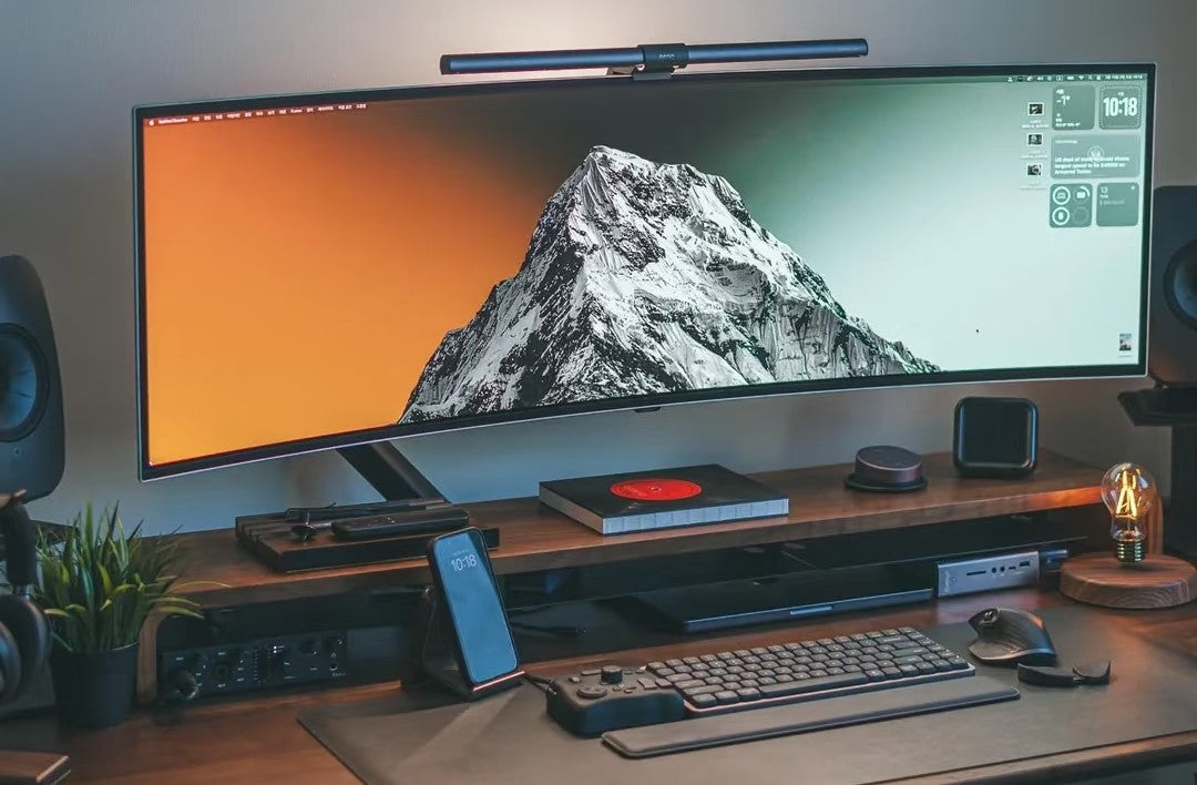 Custom wide monitor riser supporting an ultrawide display on a minimal desk setup with chrome steel and acrylic construction