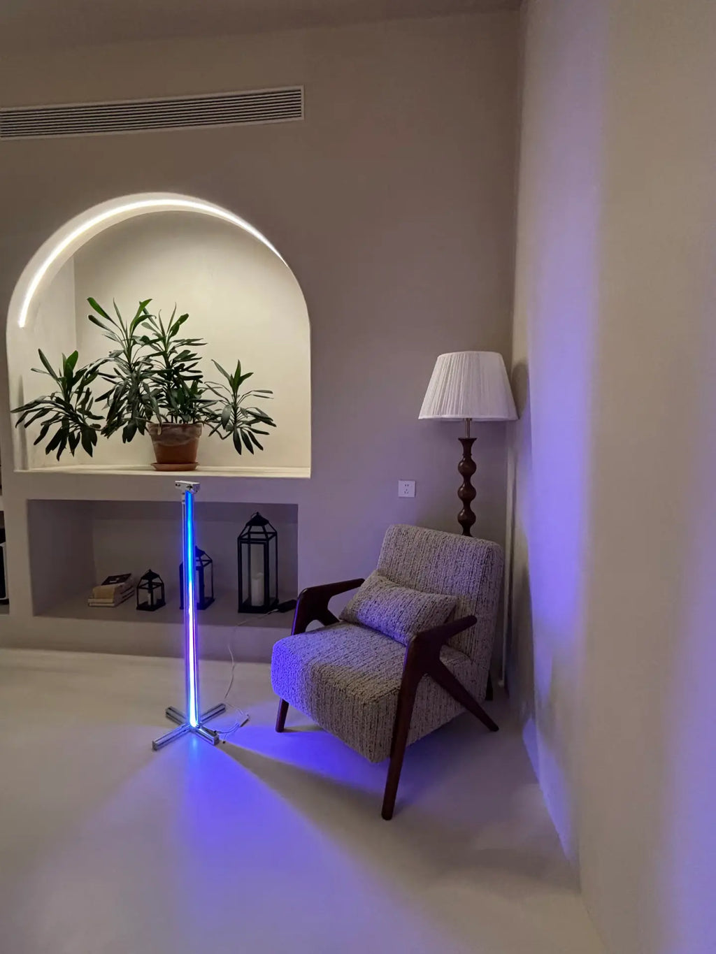 HushLume RGB Corner Floor Lamp glowing blue in a living room corner beside an armchair and arched shelf with plants — ambient mood lighting