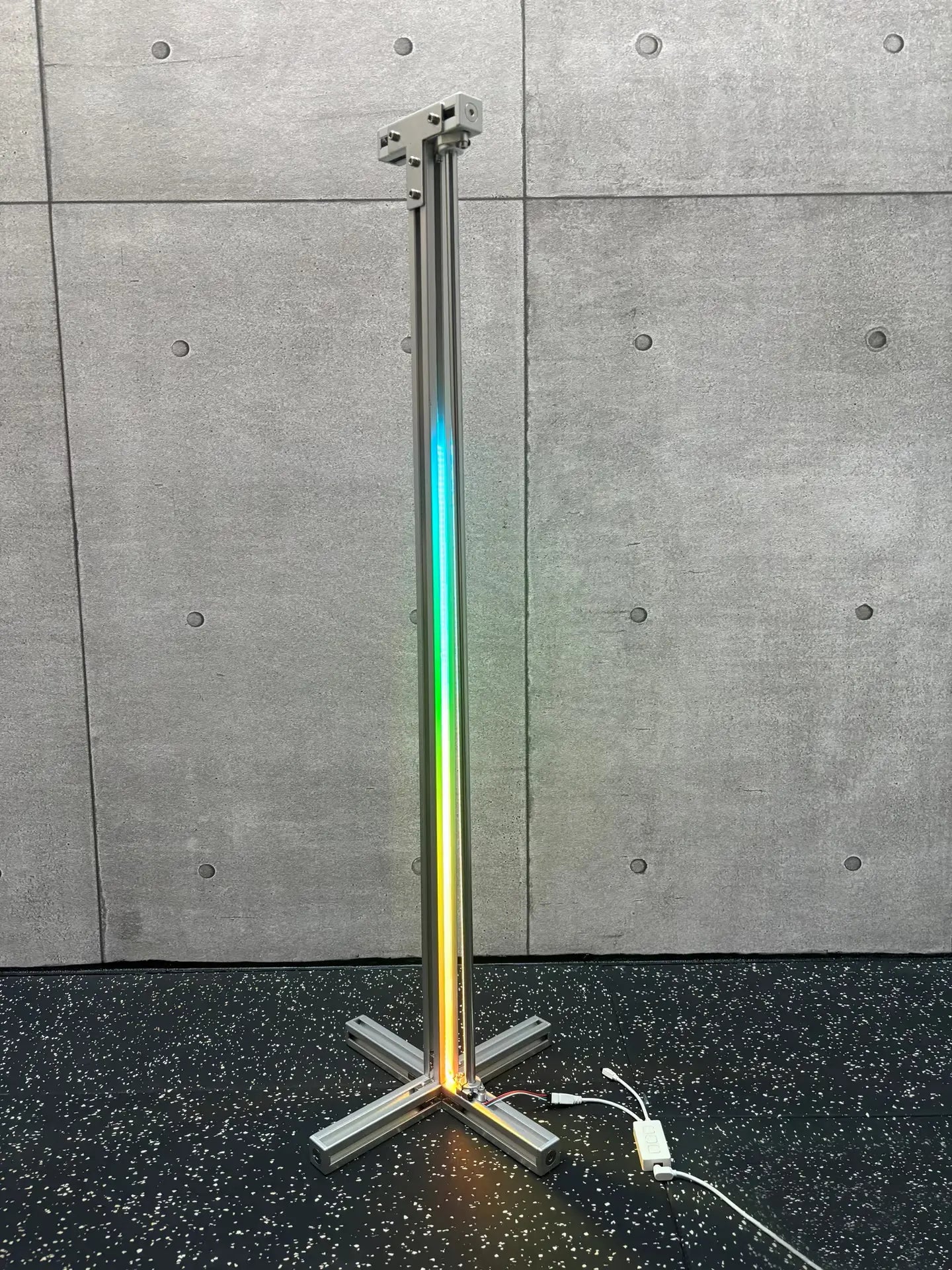 HushLume RGB Corner Floor Lamp full-spectrum rainbow gradient on 3030 aluminum frame against concrete wall — industrial build quality