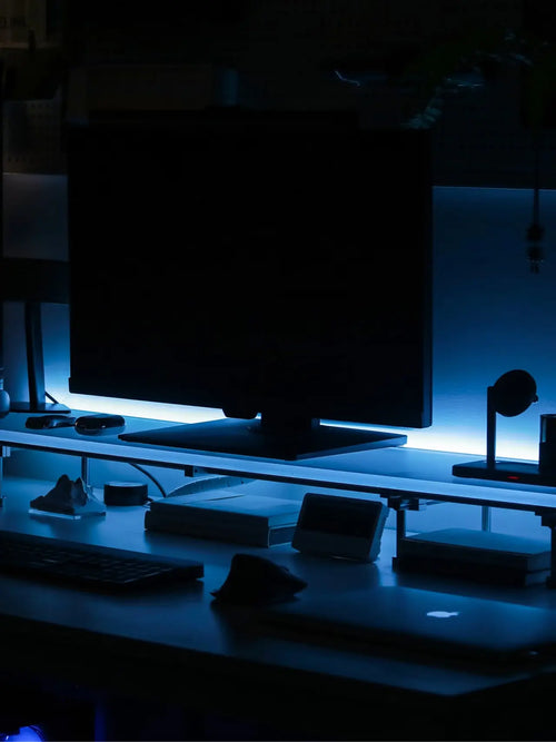 HushLume custom monitor riser with blue ambient lighting on dark desk setup — chrome steel & acrylic display shelf