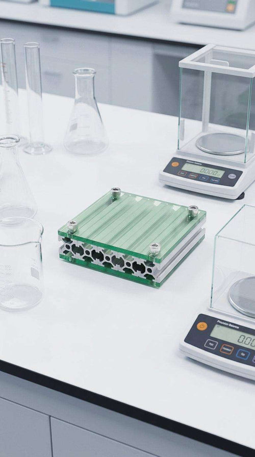 HushLume 10x10cm industrial aluminum coaster with translucent green acrylic plates, styled in a minimalist laboratory setup with science equipment.