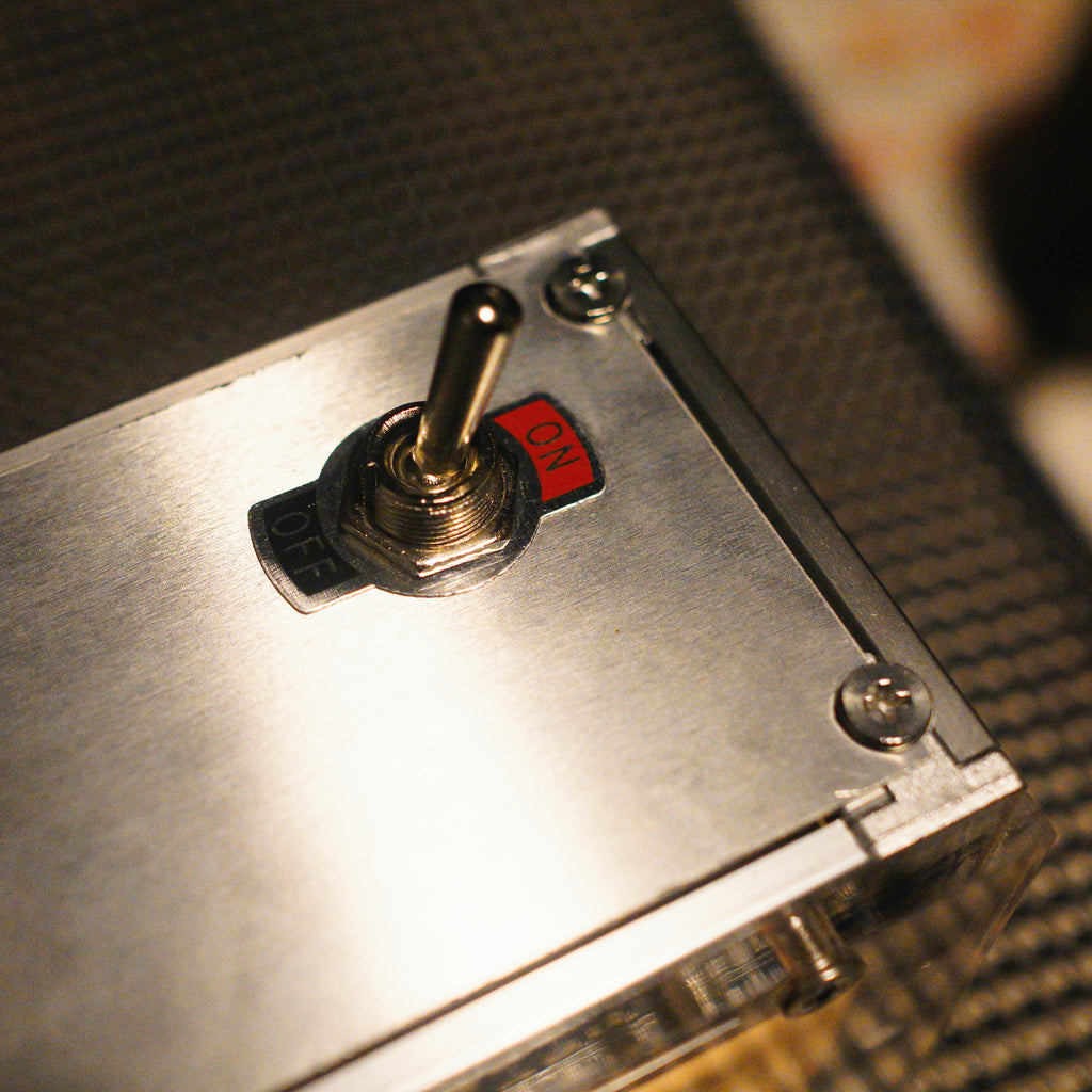 Macro close-up of the metal toggle switch with ON/OFF labels on the brushed aluminum chassis of the HushLume smart industrial light box.