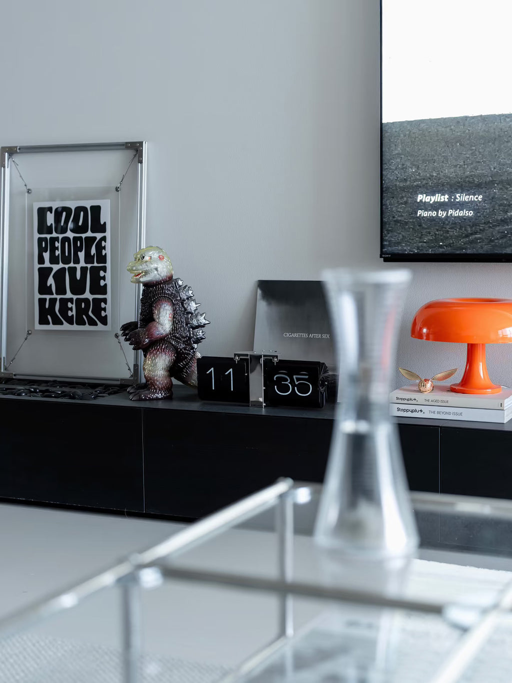 Lifestyle scene of HushLume 2020 aluminum floating frame with a trendy vinyl record, vintage kaiju toy, and a bright orange mushroom lamp on a minimalist console.