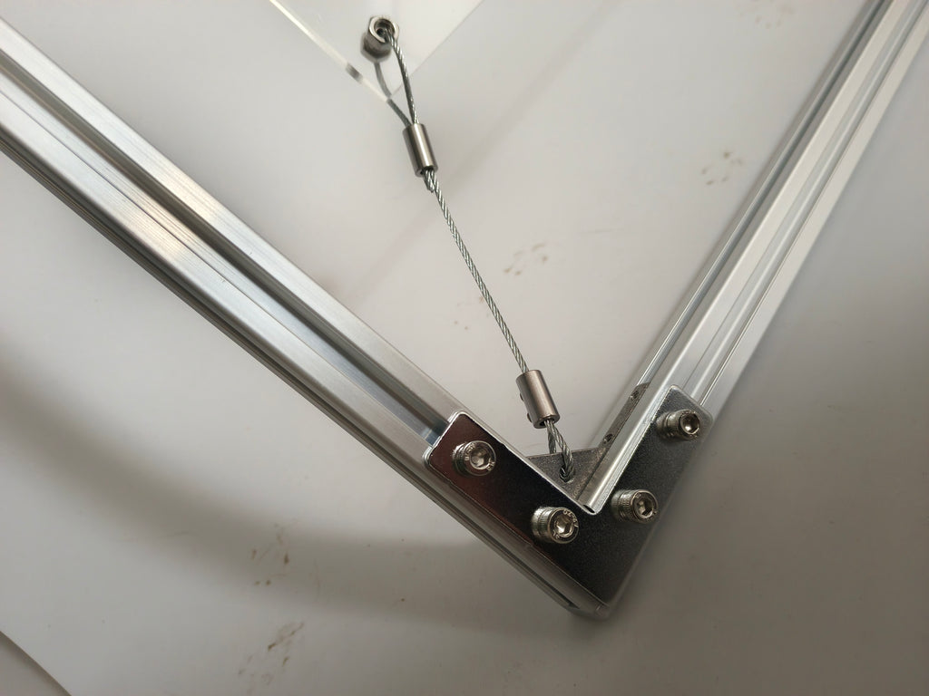 Angled close-up of HushLume industrial floating frame, showing the stainless steel tension wire fixing method on the clear acrylic panel corner.